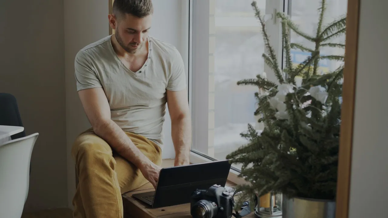 A man working on a laptop by a sunny window at home.