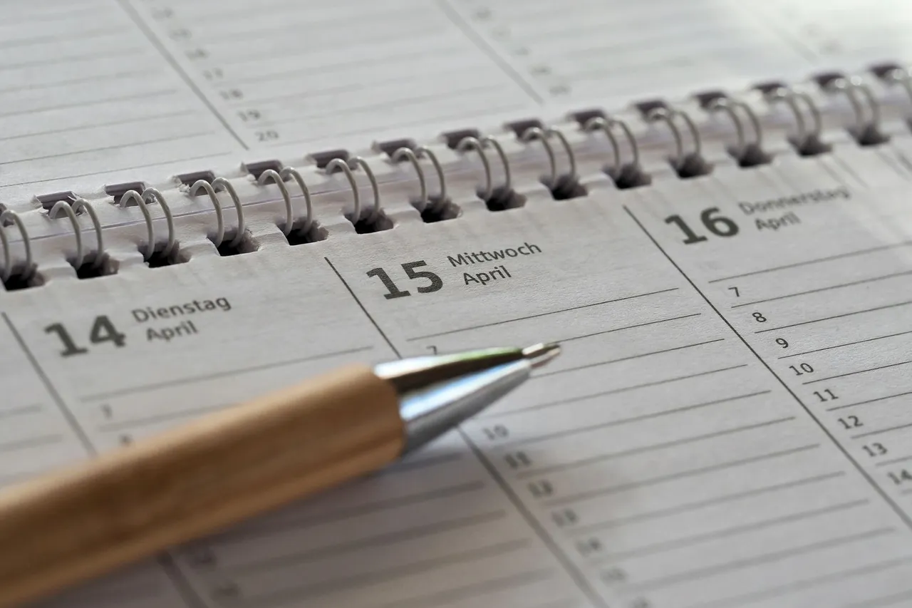 A spiral-bound calendar open to a mid-April date with a pen resting on top.
