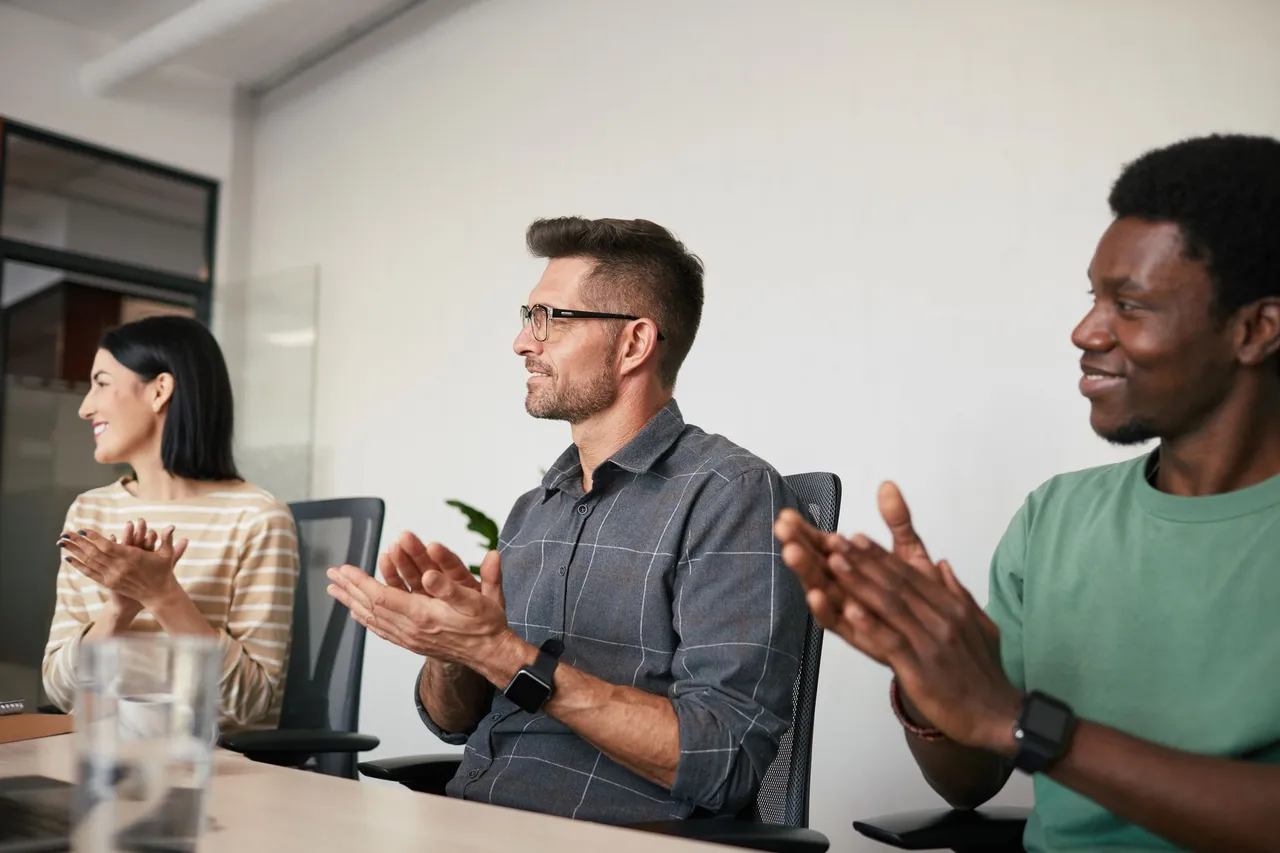 A diverse group of coworkers applauding during an office meeting, showcasing teamwork and support.