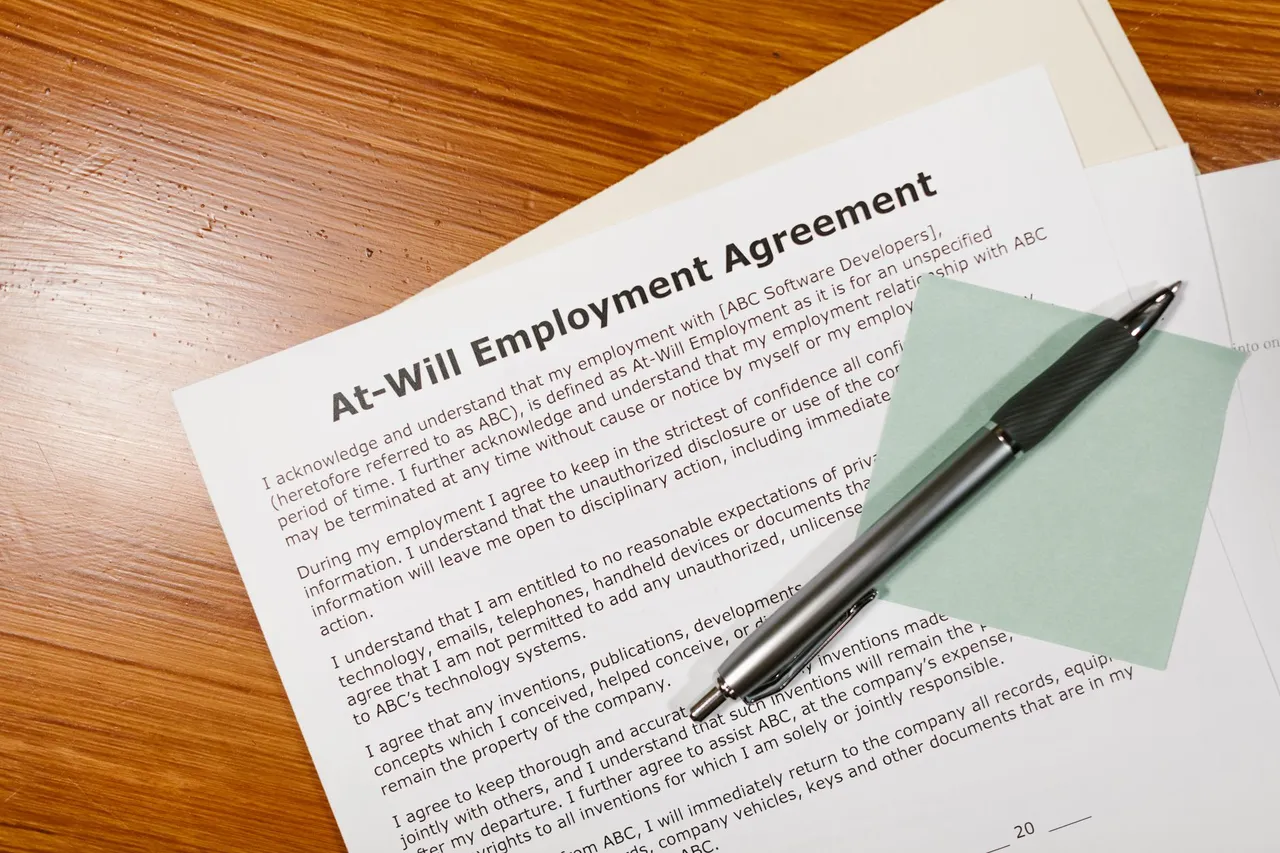 An employment agreement on a wooden desk with a black pen beside it.
