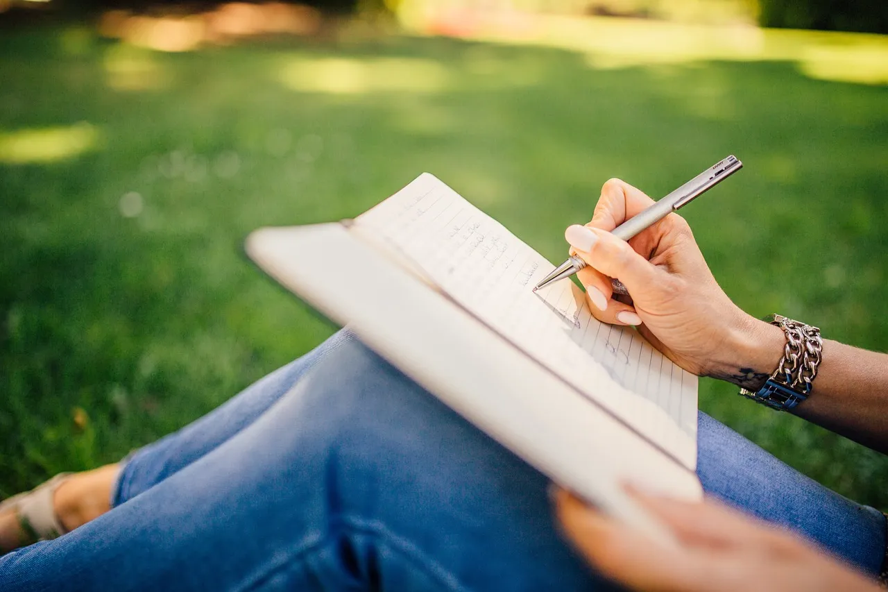 A hand writing notes with a pen in an open notebook on a desk.